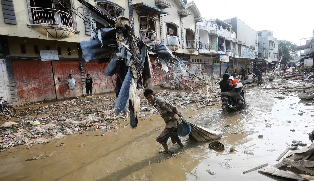 Banyak warga yang terdampak bertahan hidup dengan mendirikan tenda darurat di pinggir jalan sebagai tempat berlindung sementara karena rumah mereka rusak diterjang banjir bandang sejak akhir November 2025 lalu. Tampak dalam foto, seorang korban selamat menyeret karung berisi barang-barang yang diselamatkan melalui lumpur di area terdampak banjir bandang di Aceh Tamiang, Pulau Sumatra, Kamis 4 Desember 2025. (AP Photo/Binsar Bakkara)