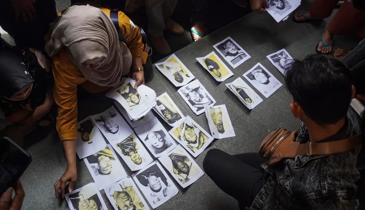 Orang-orang yang mencari anggota keluarganya memeriksa foto-foto korban kerusuhan Stadion Kanjuruhan yang disediakan oleh relawan untuk membantu mereka mengidentifikasi kerabat mereka di Malang, Jawa Timur, Minggu (2/10/2022). Sejauh ini ada 180 orang yang sedang dirawat di beberapa rumah sakit yang tersebar di beberapa rumah sakit di Malang Raya. (AP Photo/Dicky Bisinglasi)