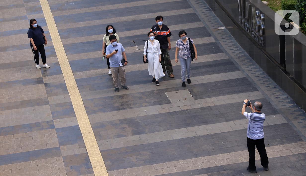 Seorang pria memotret para pejalan kaki di pedestrian kawasan Sudirman, Jakarta, Jumat (25/12/2020). Libur Natal dan Tahun Baru 2021 membuat jalanan di beberapa wilayah Ibu Kota terpantau lengang tanpa kemacetan. (Liputan6.com/Angga Yuniar)