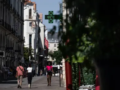 Orang-orang berjalan di jalan saat lampu apotek menunjukkan suhu turun 44 derajat celsius di Nantes, Senin (18/7/2022). Peramal cuaca menempatkan 15 departemen di sebagian besar sisi barat Prancis ke status siaga tertinggi untuk suhu ekstrem saat gelombang panas melanda negara itu dan akan mencapai puncaknya. (Loic VENANCE / AFP)
