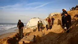 Memasuki detik-detik pergantian tahun, krisis kemanusiaan di Jalur Gaza masih sangat memprihatinkan. Tampak dalam foto, warga menyaksikan seniman Yazed Abo Jarad membuat patung pasir untuk tahun mendatang di Deir El-Balah, Jalur Gaza tengah pada 30 Desember 2025. (Bashar Taleb/AFP)