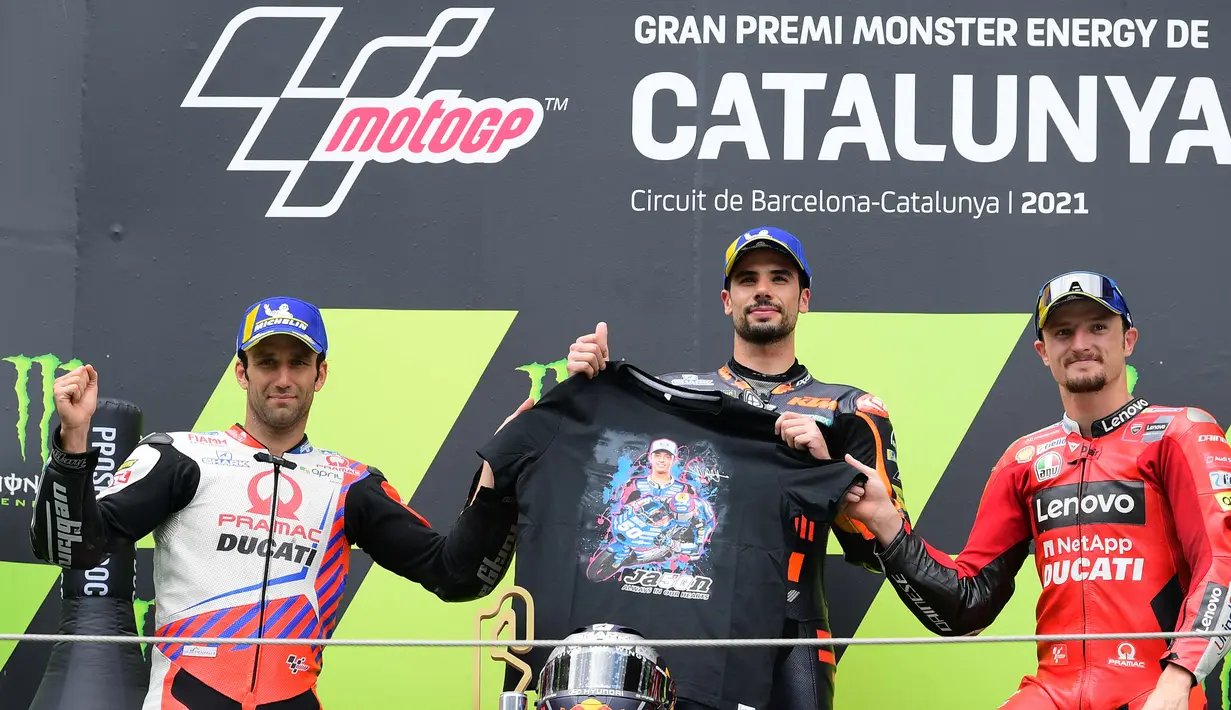 Miguel Oliviera memegang kaos bergambar pebalap Moto3 yang tewas, Jason Dupasquier bersama Johan Zarco dan Jack Miller yang finish di posisi kedua dan ketiga. (Foto: AFP/Lluis Gene)