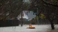 Warga menggunakan perahu kecil melintasi banjir di Christchurch, Selandia Baru, Sabtu, (22/7). Dewan Kota Christchurch mengatakan keadaan darurat setelah Sungai Heathcote meluap akibat cuaca yan buruk. (AP Photo / Mark Baker)