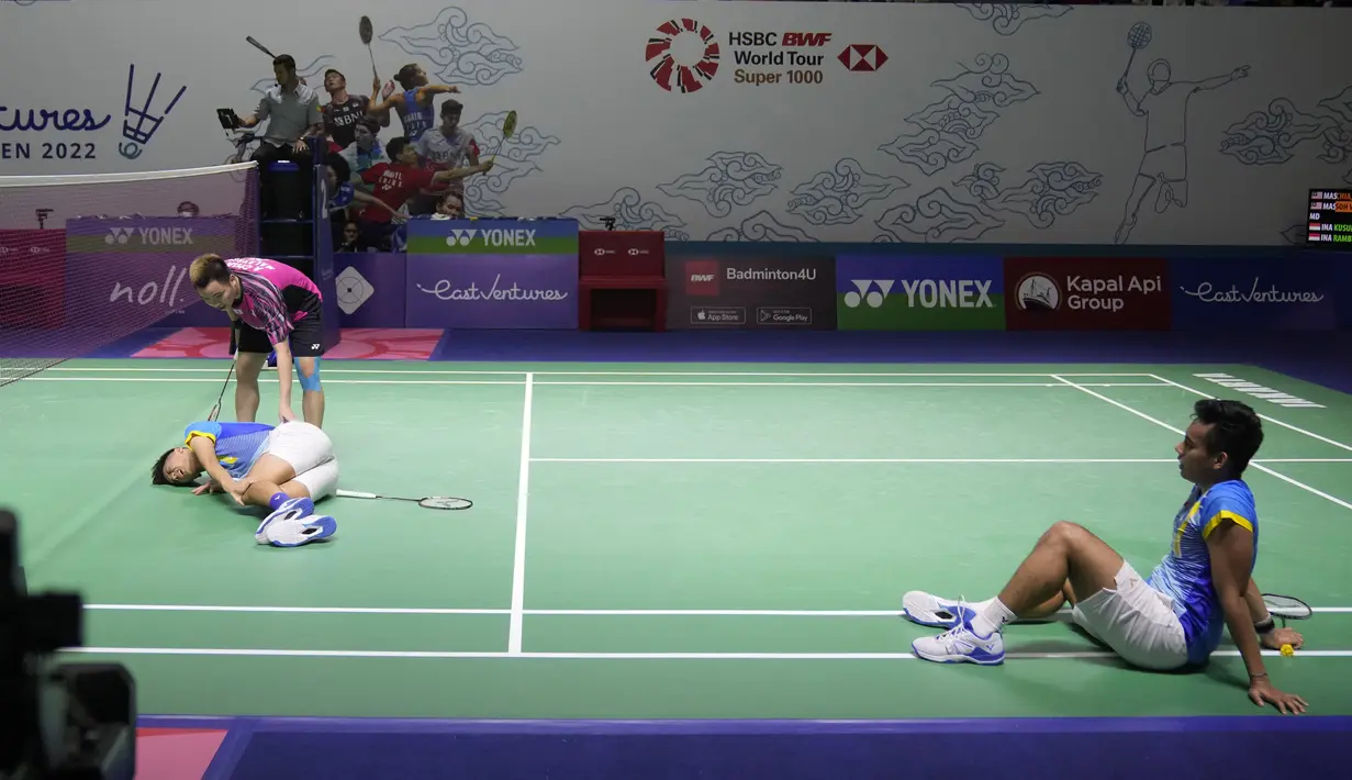<p>Ganda putra Indonesia Pramudya Kusumawardana (kanan) melihat pebulu tangkis Malaysia Aaron Chia memeriksa rekannya, Yeremia Rambitan terbaring di lapangan karena cedera lutut pada perempat final Indonesia Open 2022 di Istora Senayan, Jakarta, Jumat (17/6/2022). (AP Photo/Dita Alangkara)</p>