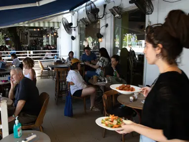 Seorang pramusaji menyajikan makanan di sebuah restoran di Tel Aviv, Israel pada Rabu (27/5/2020). Setelah lebih dari dua bulan ditutup untuk membendung penularan virus corona, restoran hingga kafe di Israel diizinkan dibuka kembali hari Rabu, 27 Mei. (AP Photo/Sebastian Scheiner)