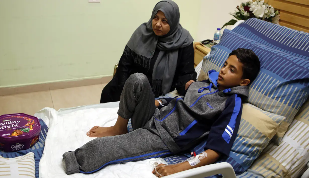 Seorang bocah Palestina, Adel Rahman Nawfal (12) berbaring di ranjang rumah sakit ditemani neneknya di kota Ramallah, Tepi Barat, Senin (23/4). Nawfal kehilangan satu kakinya akibat terkena tembakan oleh pasukan Israel. (AFP/ABBAS MOMANI)