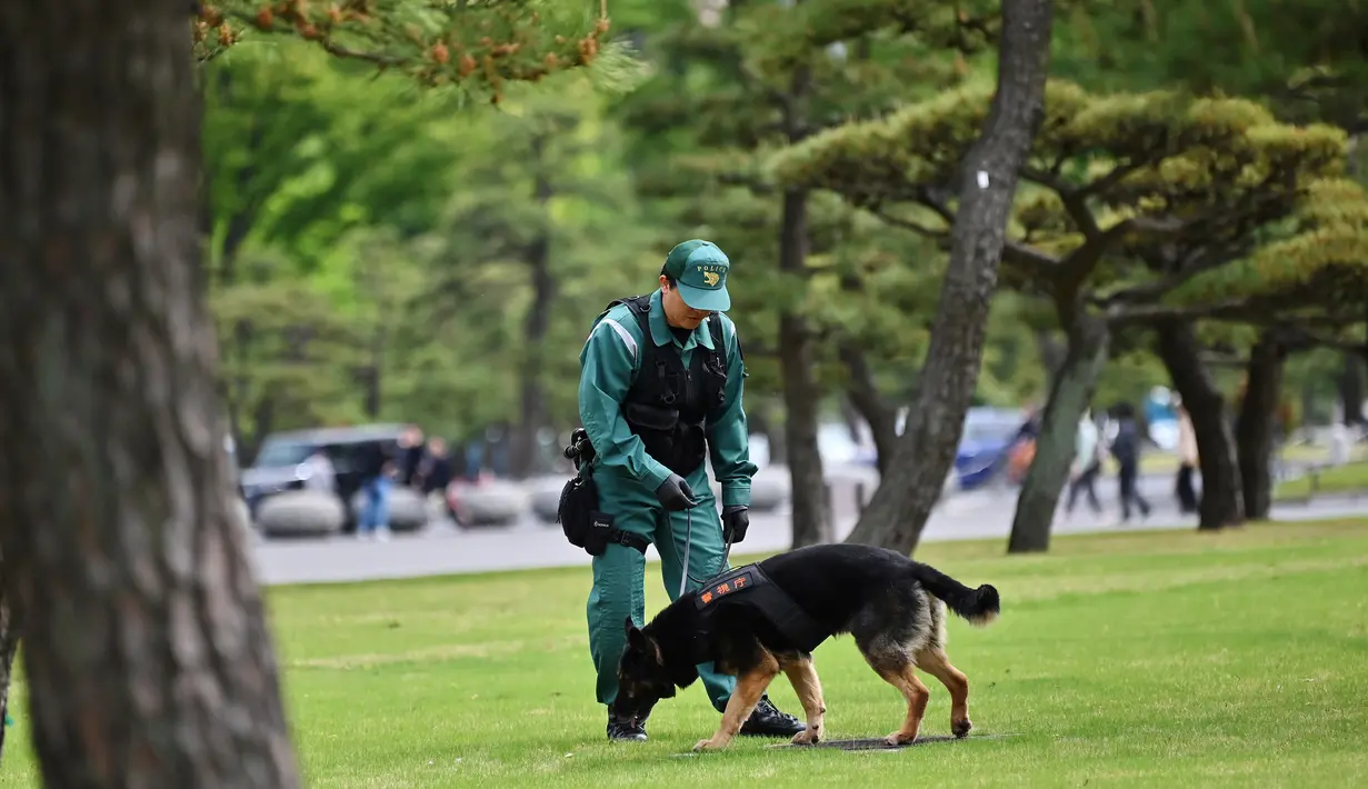 Polisi bersama anjing pelacak berkeliling di sekitar lapangan tidak jauh dari Istana Kekaisaran di Tokyo, Jepang (29/4/2019). Kaisar Jepang Akihito akan turun dari Tahta Krisan pada 30 April 2019 mengakhiri 30 tahun masa pemerintahannya. (Charly Triballeau / AFP)