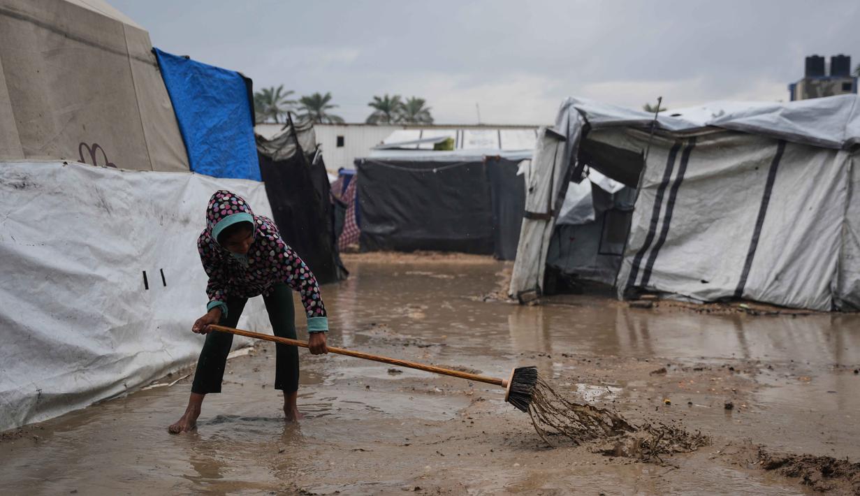 Diketahui, serangan militer Israel telah menghancurkan 92 persen bangunan tempat tinggal di Gaza. Tampak dalam foto, Samar Fayyad, 12 tahun, mencoba membersihkan air di luar tenda keluarganya yang terendam banjir di kamp sementara untuk pengungsi Palestina setelah hujan deras di Deir al-Balah, Jalur Gaza tengah, Selasa 25 November 2025. (AP Photo/Abdel Kareem Hana)