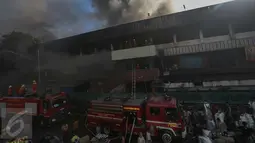 Petugas pemadam kebakaran berusaha memadamkan api sementara sejumlah pedagang terlihat sibuk menyelamatkan barang dagangan mereka yang masih ada di dalam Pasar Senen, Jakarta Pusat, Kamis (19/1). (Liputan6.com/Faizal Fanani)