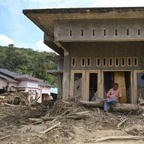 Permukiman warga nyaris hilang dan hancur, rata dengan lumpur. Tampak dalam foto, seorang warga duduk di depan rumahnya yang rusak akibat banjir bandang di Garoga, Provinsi Sumatera Utara, pada Kamis 4 Desember 2025. (YT HARIONO/AFP)