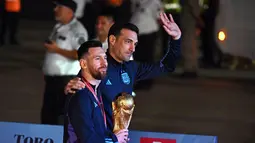 Kapten Argentina Lionel Messi (kiri) memegang Trofi Piala Dunia 2022 bersama pelatih Lionel Scaloni setibanya di Bandara Internasional Ezeiza di Ezeiza, provinsi Buenos Aires, Argentina (20/12/2022). Argentina mengakhiri penantian juara usai 36 tahun. (AFP/Luis Robayo)