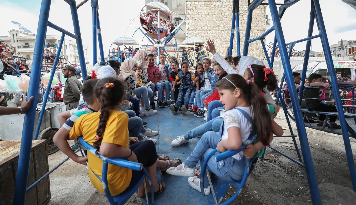 Anak-anak Suriah bermain di taman hiburan sementara ketika merayakan Idul Fitri yang menandai akhir bulan suci Ramadan di kota Idlib, Suriah, Senin (24/5/2020). Anak-anak tersebut menikmati permainan yang mungkin jarang mereka rasakan di tengah peperangan yang masih berkecamuk. (OMAR HAJ KADOUR/AFP)