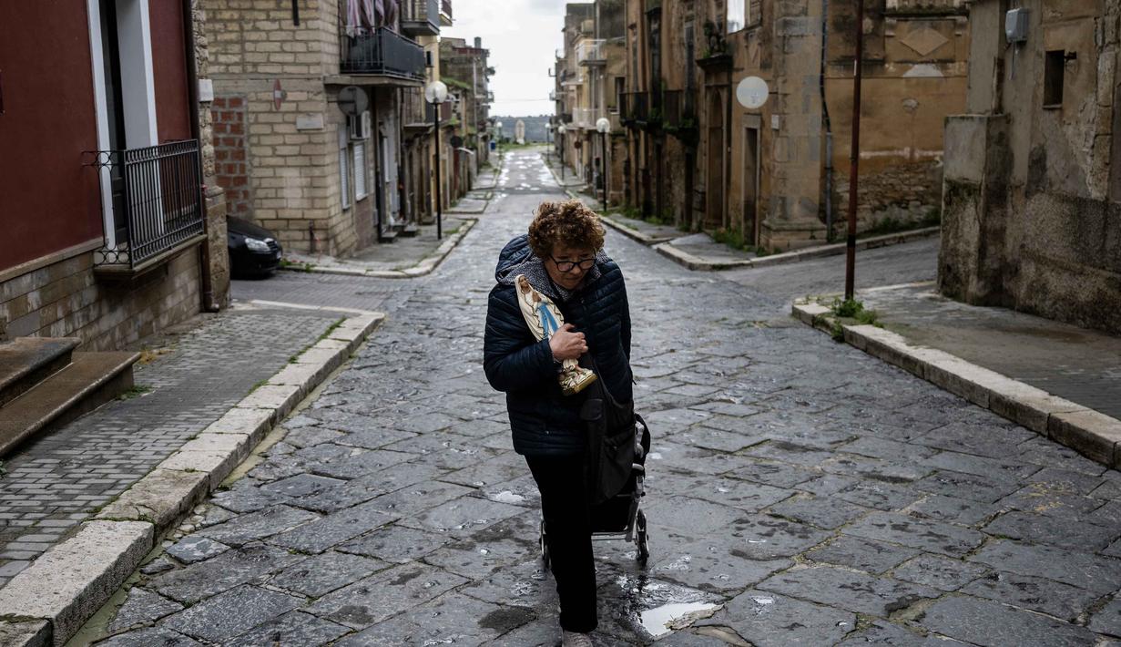 Pemerintah Italia telah mengalokasikan dana darurat nasional sebesar 100 juta Euro atau sekitar Rp1,7 triliun yang akan digunakan untuk pembersihan puing-puing, pemulihan layanan publik esensial, serta bantuan kemudahan bagi penduduk yang terdampak di tiga wilayah selatan yang berada dalam status darurat selama satu tahun ke depan. Tampak dalam foto, seorang wanita memegang patung Bunda Maria saat meninggalkan rumahnya setelah kembali bersama petugas pemadam kebakaran untuk mengambil barang-barangnya di zona merah Niscemi, Sisilia, Kamis 29 Januari 2026. (MARCO BERTORELLO/AFP)