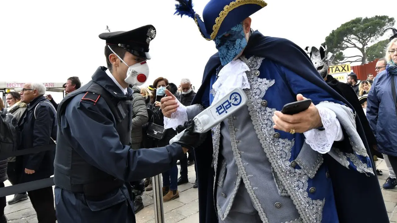 Seorang polisi yang mengenakan masker sanitasi mengontrol dengan detektor logam pada acara karnival di Venesia, Minggu, 23 Februari 2020.