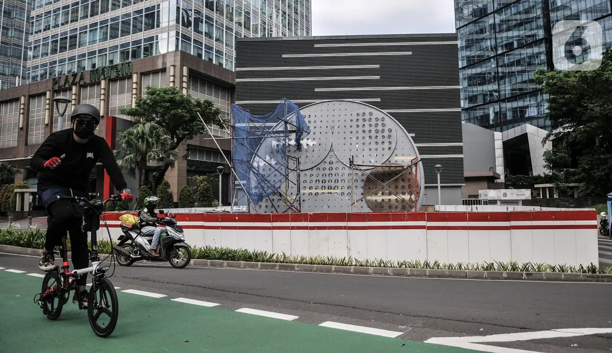 Pesepeda saat melintas di depan proyek pembangunan Tugu Sepeda di Jalan Jenderal Sudirman, Jakarta, Senin (5/4/2021). Pembangunan tugu ini berbentuk satu buah ban sepeda berukuran raksasa. (merdeka.com/Iqbal S. Nugroho)