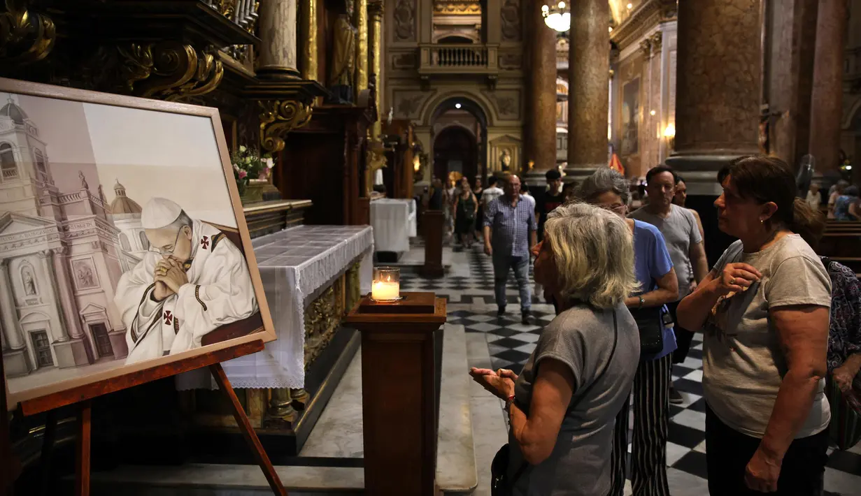 Para wanita melihat lukisan yang menggambarkan Paus Fransiskus di Basilika San Jose de Flores di Buenos Aires pada 23 Februari 2025. (Emiliano Lasalvia/AFP)