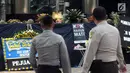 Petugas kepolisian mengamati karangan bunga dekat kain hitam besar yang menutupi logo KPK di Gedung Merah Putih, Jakarta, Senin (9/9/2019). Keberadaan kain hitam dan karangan bunga ini merupakan bentuk protes atas revisi Undang-undang KPK yang dinilai dapat melemahkan KPK. (merdeka.com/Dwi Narwoko)