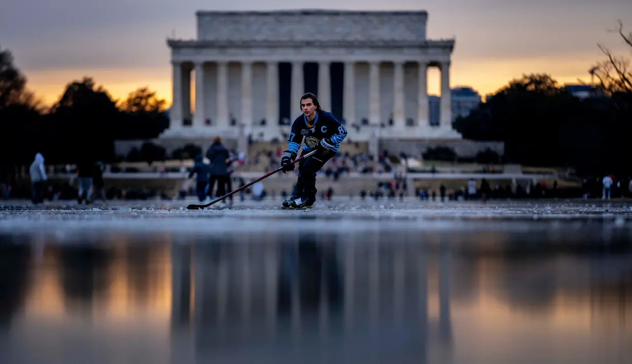 Lincoln Memorial terlihat saat Jacek Zavora (21) dari Arlington bermain hoki di Reflecting Pool yang membeku, National Mall, Washington, Amerika Serikat, 26 Desember 2022. Banyak warga memposting pengalaman tersebut ke media sosial. (AP Photo/Andrew Harnik)
