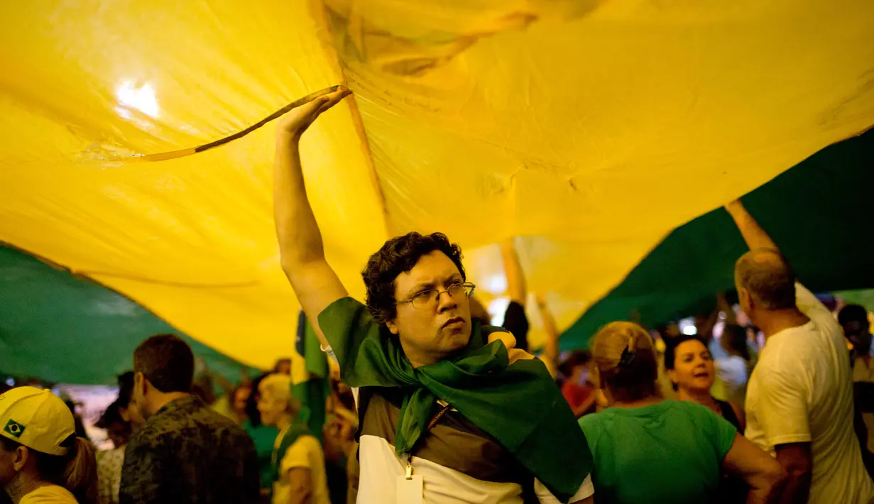 Demonstran membentangkan bendera Brasil saat menggelar aksi protes di Rio de Janeiro, Brasil (3/4). Sebelumnya, mantan Presiden Brasil Luiz Inacio Lula da Silva terbukti melakukan korupsi, dan menerima suap. (AP / Silvia Izquierdo)