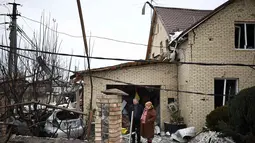 Serangan menyebabkan kerusakan parah di beberapa lokasi. Tampak dalam foto, warga setempat berdiri di antara puing-puing di halaman rumah yang rusak akibat serangan udara di Sofiivska Borshchagivka, wilayah Kyiv pada Minggu 22 Februari 2026. (Henry NICHOLLS/AFP)