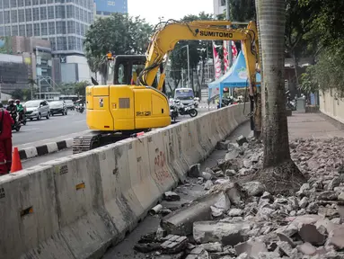 Pekerja dibantu alat berat merevitalisasi trotoar di kawasan Bundaran HI, Jakarta Pusat, Senin (15/7/2019). Penantaan ini dilakukan untuk mempercantik trotoar dan memberikan rasa nyaman bagi pejalan kaki. (Liputan6.com/Faizal Fanani)