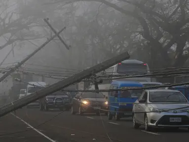 Sejumlah kendaraan melewati tiang listrik yang roboh akibat angin kencang yang disebabkan Topan Nock-ten di kota Pili, Camarines sur, Filipina tengah (27/12). Topan Nock-ten atau dikenal dengan Nina menerjang Filipina saat Natal. (REUTERS/Romeo Ranoco)