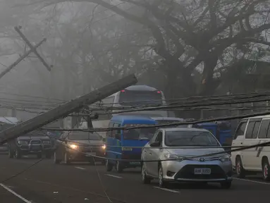 Sejumlah kendaraan melewati tiang listrik yang roboh akibat angin kencang yang disebabkan Topan Nock-ten di kota Pili, Camarines sur, Filipina tengah (27/12). Topan Nock-ten atau dikenal dengan Nina menerjang Filipina saat Natal. (REUTERS/Romeo Ranoco)