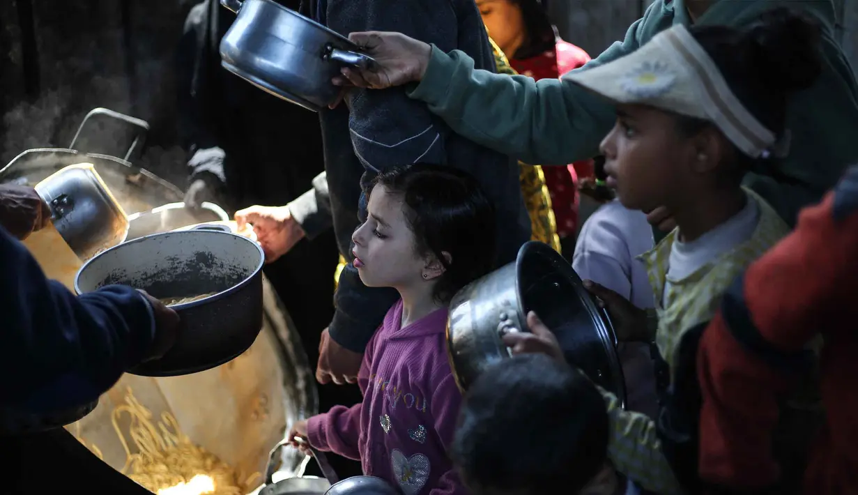 Kantor media pemerintah Gaza, pada Minggu 12 April 2026, mengatakan bahwa Jalur Gaza setiap harinya membutuhkan sekitar 450 ton, sementara pasokan yang tersedia saat ini hanya sekitar 200 ton. Tampak dalam foto, anak-anak pengungsi Palestina menerima makanan dari dapur amal di kamp pengungsi Nuseirat di Jalur Gaza tengah pada 13 April 2026. (Eyad Baba/AFP)