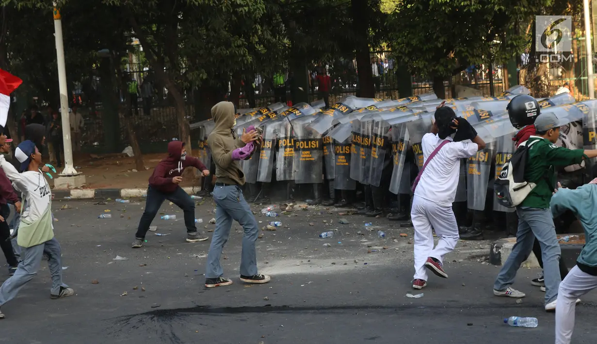Massa melempar batu ke arah polisi yang membentuk barikade dengan tameng di sekitaran Gedung DPR RI, Jakarta, Senin (30/9/2019). Kericuhan pecah lantaran massa yang kebayakan terdiri dari pelajar tersebut berusaha masuk ke area depan DPR. (Liputan6.com/Angga Yuniar)
