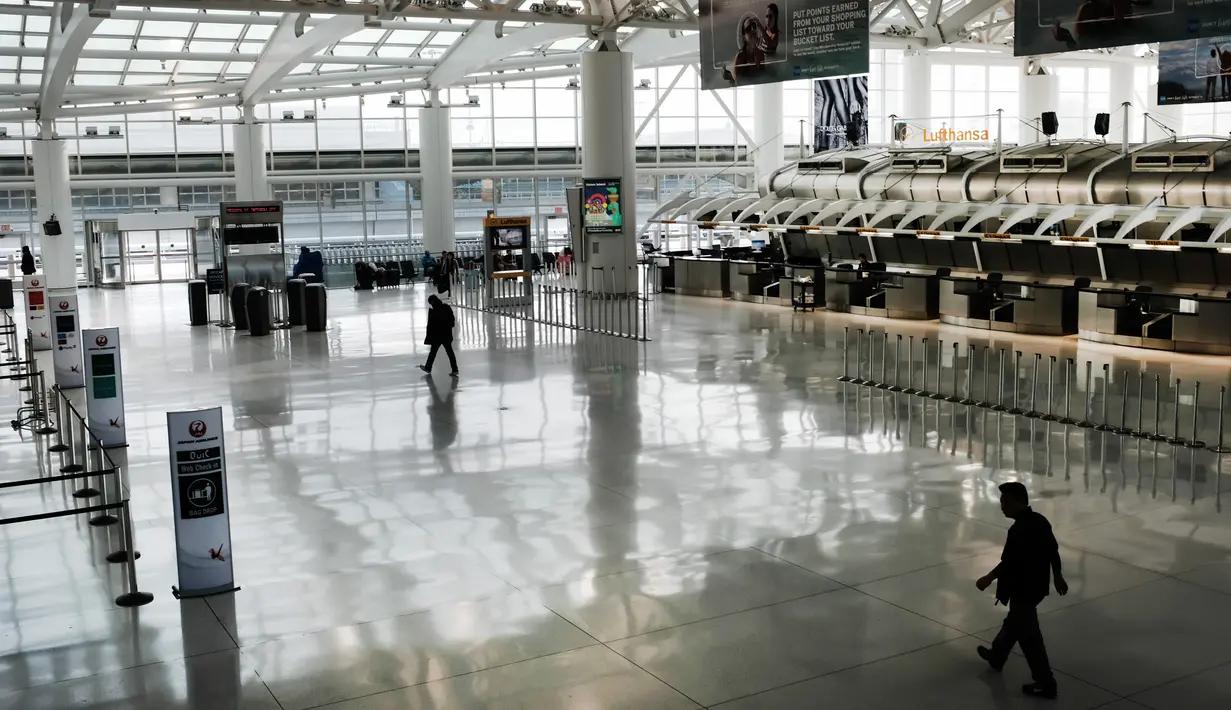 Orang-orang berjalan melalui terminal keberangkatan internasional yang sepi di Bandara John F. Kennedy (JFK), New York City, Sabtu (8/3/2020). Maskapai penerbangan terpukul wabah virus corona (COVID-19) setelah pelancong bisnis maupun rekreasi membatalkan rencana. (Spencer Platt/Getty Images/AFP)