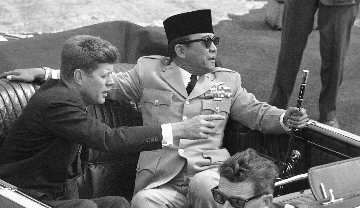 Presiden Amerika John Kennedy menunjuk Presiden Republik Indonesia Sukarno saat mereka duduk di mobil terbuka sesaat sebelum berangkat di Pangkalan Angkatan Udara Andrews, Washington, 24 April 1961. (AP Photo)