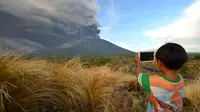 Seorang anak mengabadikan semburan abu vulkanik Gunung Agung, Karangasem, Bali, Minggu (26/11). Semburan asap dan abu vulkanik Gunung Agung mencapai ketinggian 1.500 meter dari puncak Gunung Agung. (AFP/Sonny Tumbelaka)