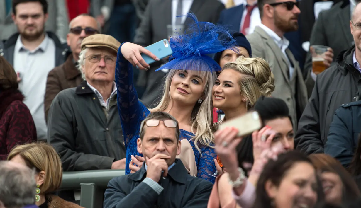 Dua racegoers terlihat berselfie saat menyaksikan Festival Grand National di arena Aintree, Liverpool, Inggris (7/4). Kehadiran racegoers memberikan nuansa tersendiri di kompetisi pacuan kuda terbesar tersebut. (AFP Photo / Oli Scarff)
