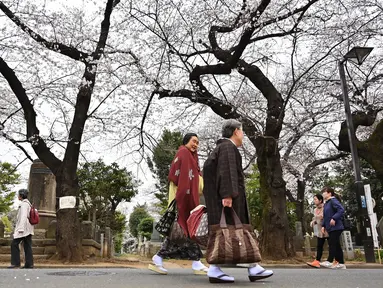Orang-orang berjalan di Pemakaman Yanaka yang dikelilingi oleh pohon sakura di distrik Taito, Tokyo, Jepang (26/3). Memasuki akhir Maret, pohon bunga sakura mulai bermekaran di sejumlah wilayah Jepang. (AFP Photo/Charly Triballeua)