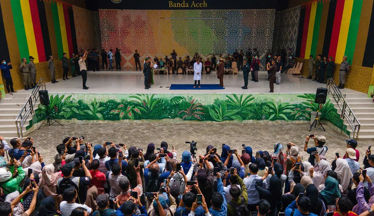 Warga menyaksikan sebelas pria dan wanita menjalani hukuman cambuk setelah dinyatakan bersalah melanggar hukum syariat Islam Aceh yang melarang hubungan seksual di luar nikah di Banda Aceh, Kamis, 20 Agustus 2026. (AFP/ Chaideer Mahyuddin)