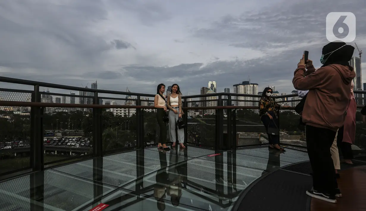 Warga berfoto saat mengisi libur Tahun Baru dengan menikmati pemandangan Kota Jakarta dari Skywalk Senayan Park, Sabtu (1/1/2022). Warga ramai-ramai datang untuk berburu foto pada spot-spot yang instagramable di Skywalk Senayan Park. (Liputan6.com/Johan Tallo)