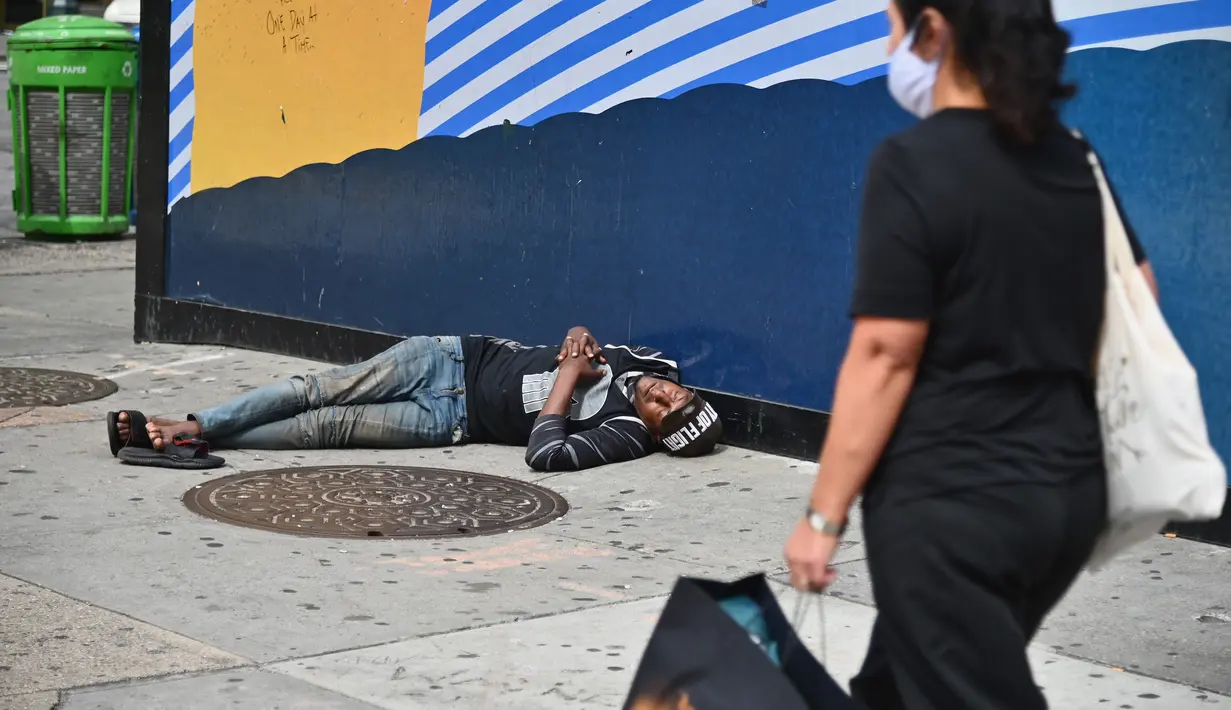 Pejalan kaki melewati seorang pria yang tidur di dekat Penn Station di Madison Square Gardens, New York City, Kamis (17/9/2020). Sejak pandemi virus corona, para tunawisma kini  lebih terlihat seiring banyaknya penutupan banyak tempat penampungan karena alasan kesehatan. (Angela Weiss / AFP)