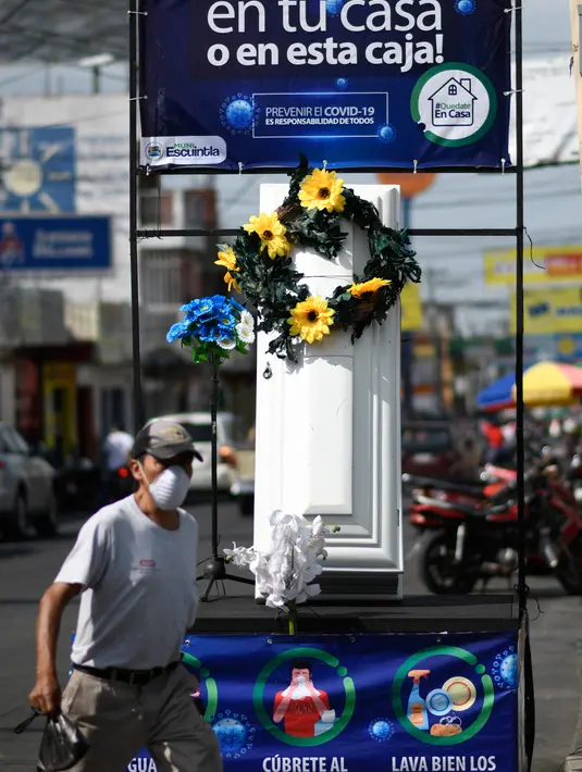 Warga berjalan dekat peti mati dengan tulisan, "Anda memutuskan, di rumah atau di dalam kotak ini", sebagai bagian dari kampanye pemerintah setempat di jalan-jalan kotamadya Escuintla, Guatemala City pada 21 Juli 2020. Kampanye itu sebagai upaya menghentikan penyebaran COVID-19. (Johan ORDONEZ/AFP)