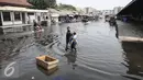 Warga melintasi genangan banjir di pasar ikan Pelabuhan Muara Baru, Penjaringan, Jakarta, (7/6). Banjir rob terjadi akibat jebolnya tanggul di sisi Timur Pelabuhan Muara Baru hingga meluapnya air yang mencapai sekitar 50 cm. (Liputan6.com/Faizal Fanani)