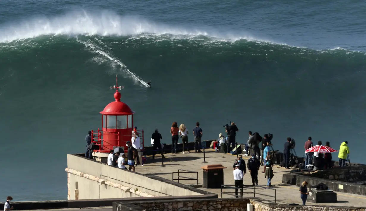 Orang-orang di atas mercusuar menyaksikan peselancar menunggangi ombak selama sesi selancar derek di Praia do Norte atau Pantai Utara di Nazare, Portugal, Kamis (29/10/2020). (AP Photo/Pedro Rocha)