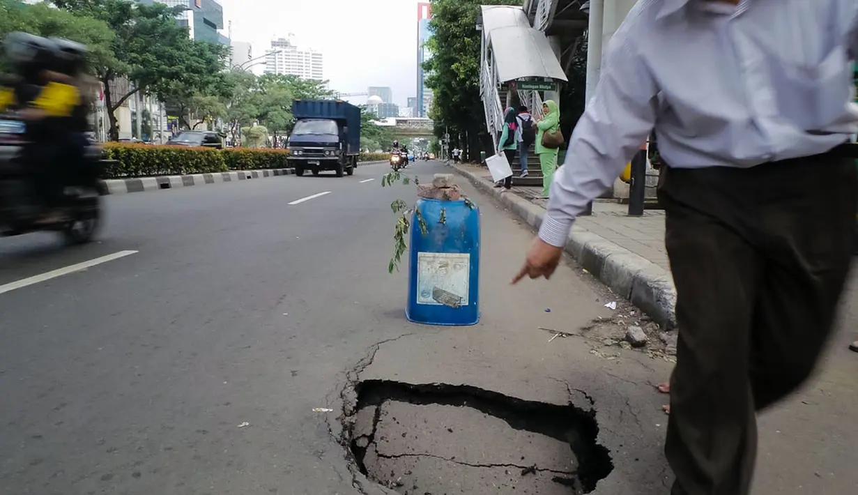Salah satu warga melintasi sisi jalan yang amblas di depan Wisma Bakrie, Kuningan, Jakarta, (12/8/2014). (Liputan6.com/Faizal Fanani)