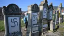 Seorang wanita berjalan di dekat nisan yang menjadi sasaran vandalisme di pemakaman Yahudi, Westhoffen, dekat Strasbourg, Prancis, Rabu (4/12/2019). Sedikitnya 107 makam menjadi sasaran vandalisme dengan dicoreti lambang swastika Nazi. (AFP/Patrick Hertzog)