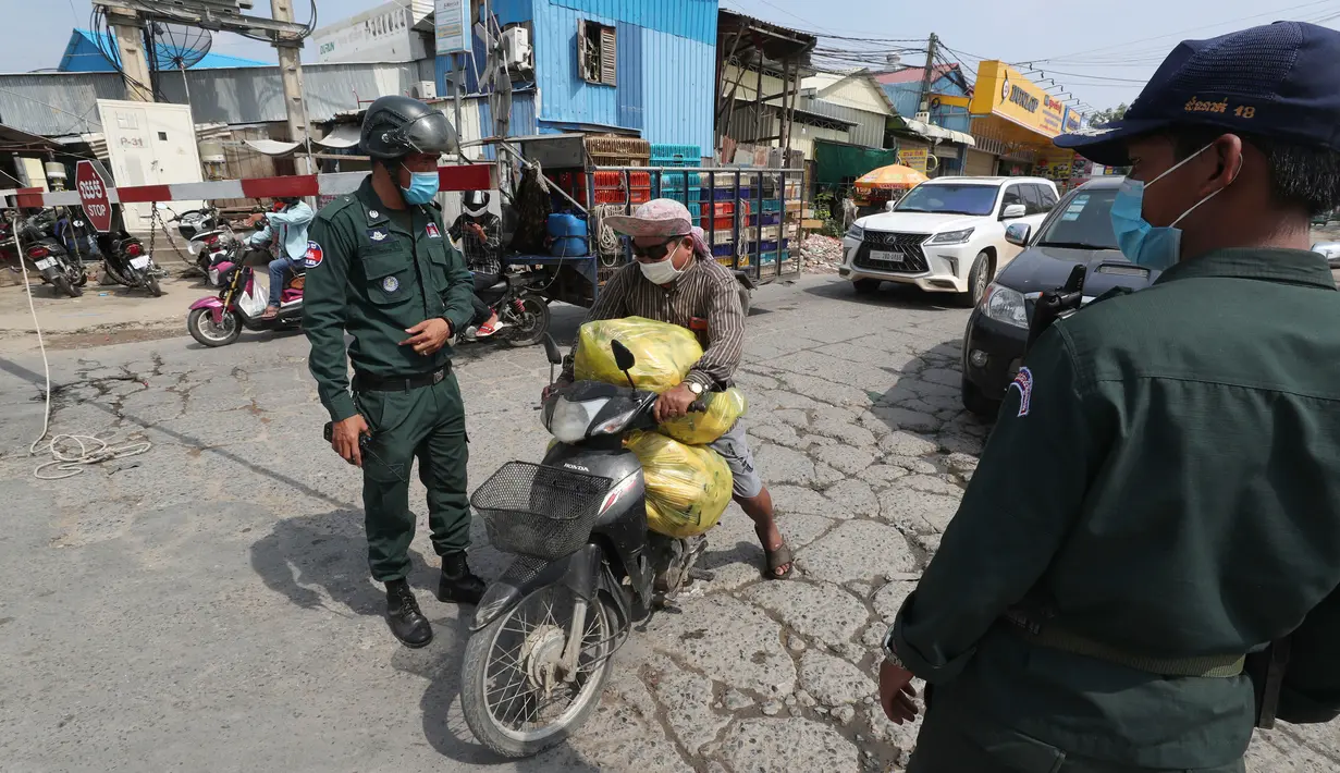 Pedagang membawa ayam mati untuk pasar terdekat saat polisi setempat berjaga di jalan yang diblokir dekat bandara Internasional Phnom Penh, Kamis (15/4/2021). Pemimpin Kamboja memutuskan untuk lockdown Phnom Penh selama dua minggu menyusul kenaikan tajam kasus COVID-19. (AP Photo/Heng Sinith)