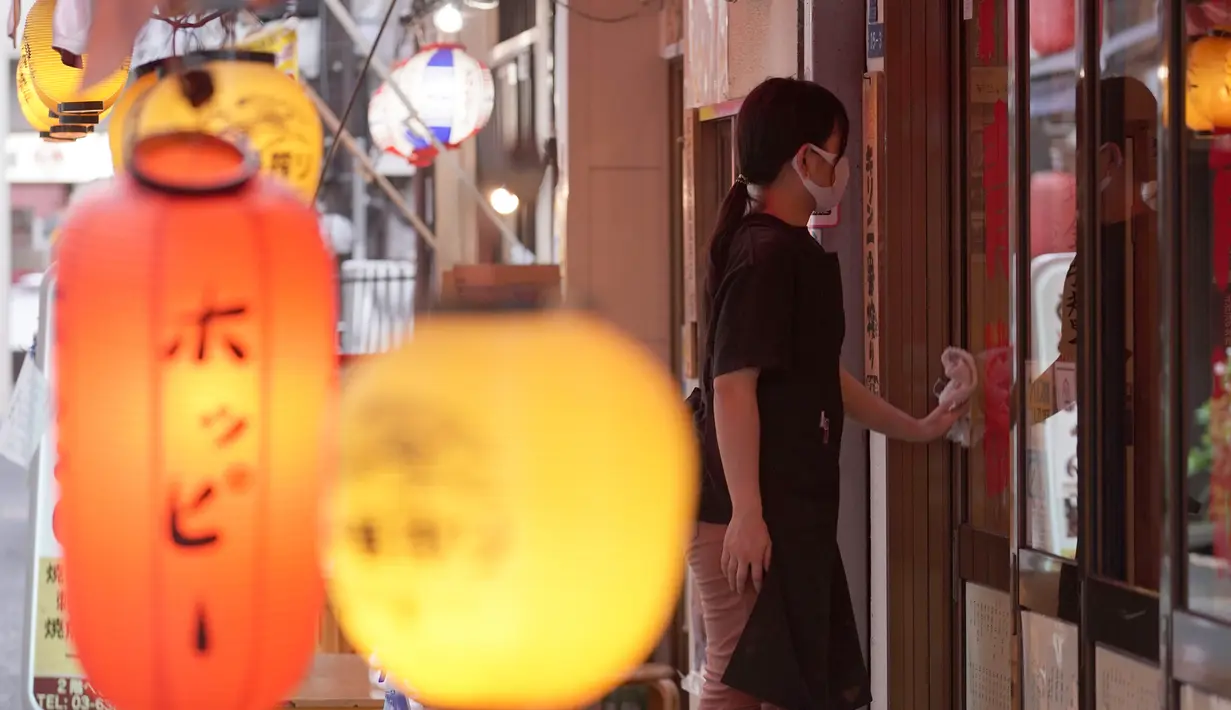 Seorang pekerja mengenakan masker mencegah penyebaran coronavirus baru membersihkan jendela sebuah pub Jepang di Tokyo, Senin, (20/7/2020). Ibukota Jepang hari Senin mengkonfirmasi lebih dari 160 kasus virus corona baru. (AP Photo/Eugene Hoshiko)