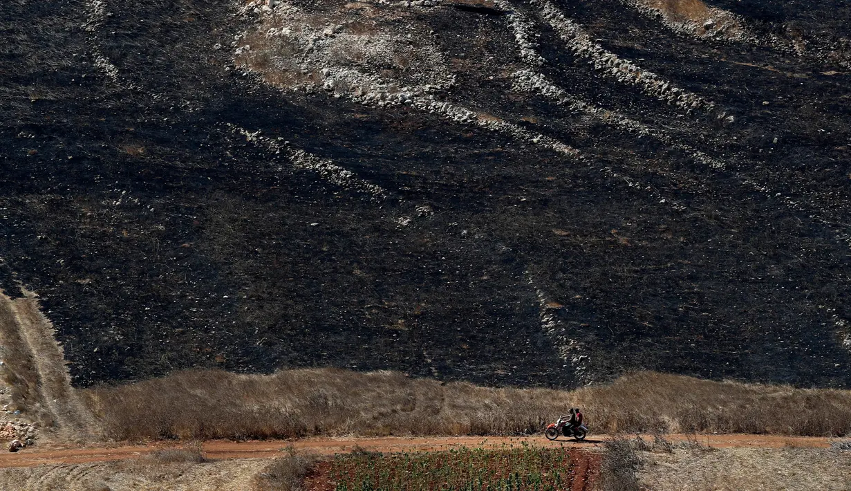 Warga Lebanon mengendarai sepeda motor melewati ladang yang terbakar usai serangan Israel di desa perbatasan Maroun Al-Ras, Lebanon, Senin (2/9/2019). Serangan artileri Israel menyebabkan kebakaran lahan di Lebanon. (AP Photo/Hussein Malla)
