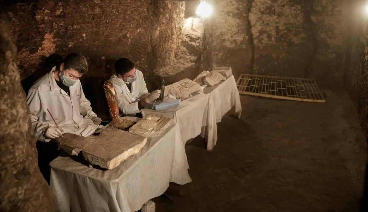 Arkeolog meneliti patung-patung dan artefak yang ditemukan di dalam sebuah makam kuno dekat piramida terkenal Mesir di Saqqara, Giza, Sabtu (10/11). Puluhan mumi kucing dan koleksi langka scarab telah ditemukan di tujuh sarkofagus. (AP/Nariman El-Mofty)