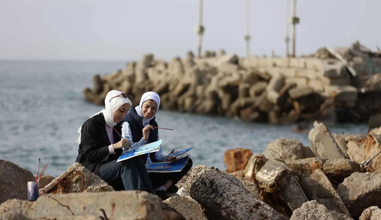Lokakarya ini memberi ruang untuk memproses trauma melalui warna dan kreativitas. Tampak dalam foto, para perempuan muda berinteraksi sambil melukis di pelabuhan Kota Gaza pada Kamis 12 Februari 2026. (Omar AL-QATTAA/AFP)