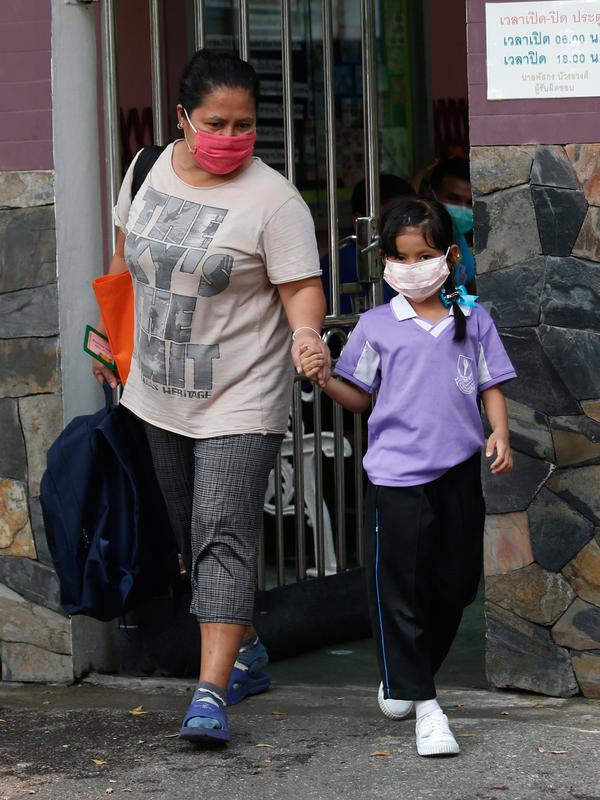 Seorang anak laki-laki mengenakan masker saat dijemput orang tuanya di Bangkok (30/1). Kementerian Kesehatan Thailand memberi peringatan kepada warga dan turis untuk menghindari kegiatan di ruang terbuka dan mengenakan masker. (AP Photo/Sakchai Lalit)