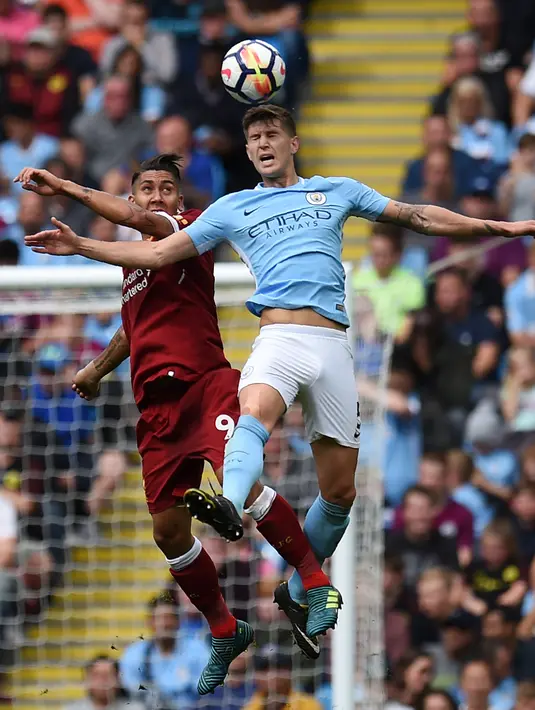 Pemain Manchester City John Stones berebuta boal diudara dengan Roberto Firmino saat pertandingan Manchester City menjamu Liverpool di Stadion Etihad, Manchester (9/9). (AFP Photo/Oli Scarff)