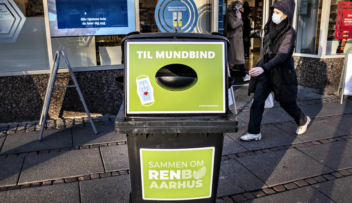 Seorang pejalan kaki berjalan melewati tempat sampah untuk masker sekali pakai, di Aarhus Center, Denmark, Senin (23/11/2020). Kota Aarhus menempatkan seratus tempat sampah khusu berukuran 240 liter yang dapat menampung sekitar 3000 masker bekas. (Henning Bagger/Ritzau Scanpix/AFP)